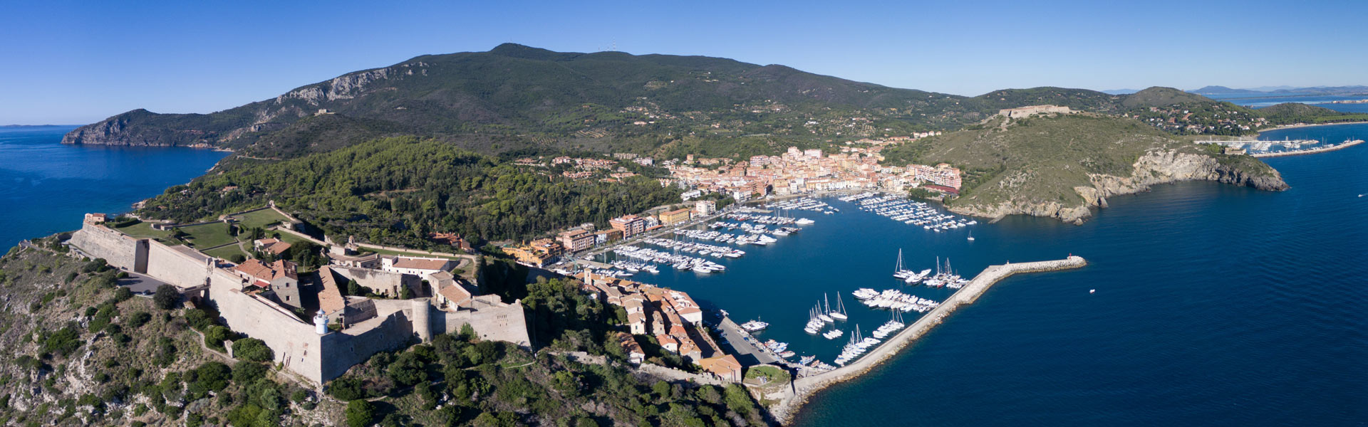 La foto rappresenta il paese di Porto Ercole visto dall'alto. Sullo sfondo il Monte Argentario ed al lato destro si scorge una parte del porto di Cala Galera.
